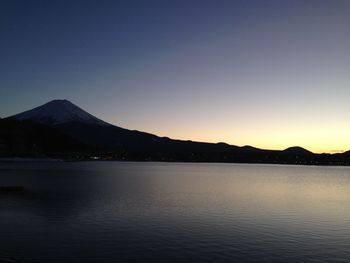 Scenic view of lake by silhouette mountains against clear sky