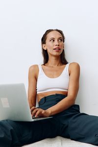 Portrait of young woman using laptop while sitting against white background