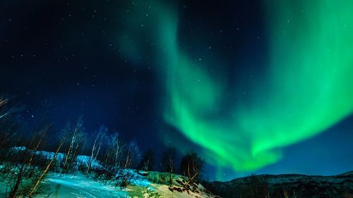 Scenic view of mountains against aurora borealis in sky at night