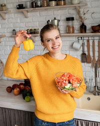Portrait of smiling woman holding yellow bell pepper in kitchen