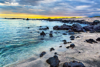 Scenic view of rocks at shore during sunset