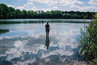Rear view of woman standing in lake with clouds reflection