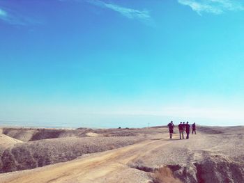 Men walking on dirt road against blue sky on sunny day