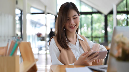Smiling businesswoman using smart phone sitting at cafe