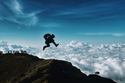 Man jumping on top of mountain against sky