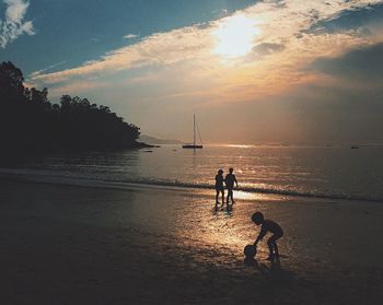 Silhouette people playing on beach against sky during sunset