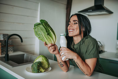 Smiling woman holding vegetable standing at home