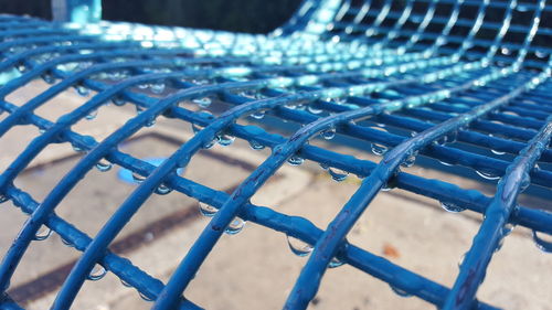 Close-up of blue metallic bench with raindrops on footpath