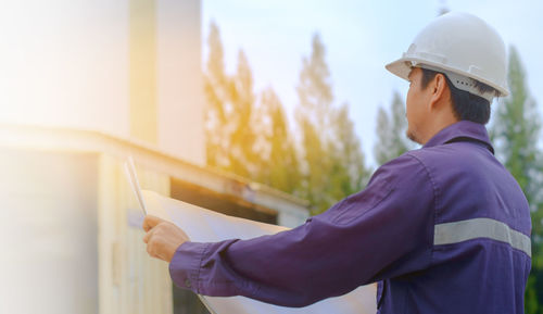 Man holding hat standing against built structure