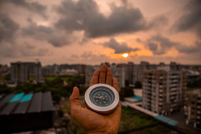 Midsection of man holding cityscape against sky during sunset