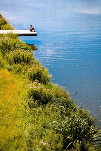 Mid distance view of man sitting on pier over lake