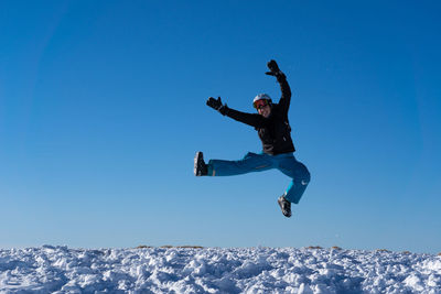 Full length of man jumping against clear blue sky