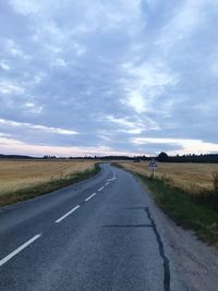 Empty road amidst field against sky