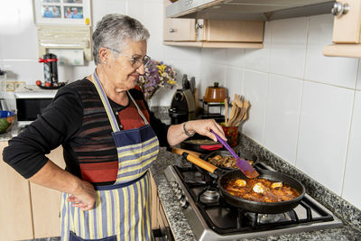 Old lady in the kitchen cooking food.