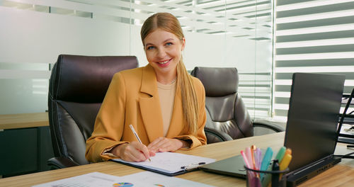 Business woman signing a contract with a pen and looking in camera. 