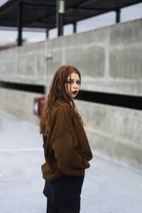 Side view portrait of woman standing against concrete wall