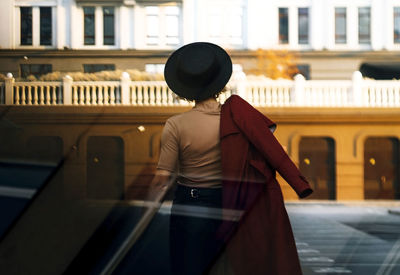 Back view woman walking on city street at sunset wearing hat and coat