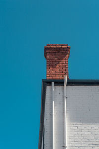 Low angle view of chimney on house against clear blue sky