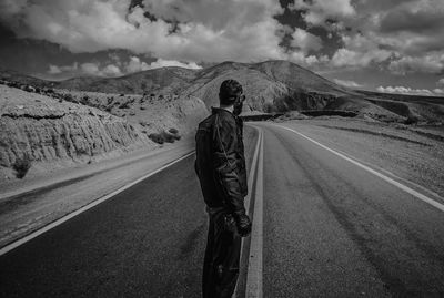 Rear view of man standing on mountain road against cloudy sky