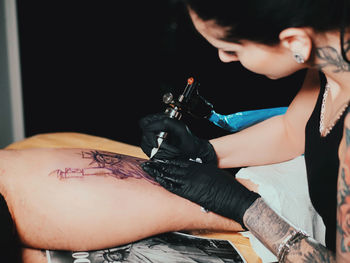 Young woman tattooing statue of liberty man on calf at parlor