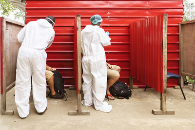 Back view of unrecognizable african male medics in protective uniforms taking pcr test sample from anonymous travelers in red cabins in countryside