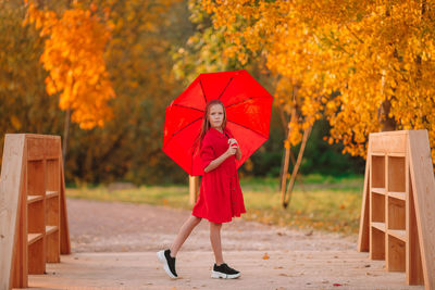 Full length of girl holding red umbrella standing at park