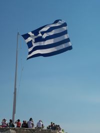 People at observation point with greek flag against sky