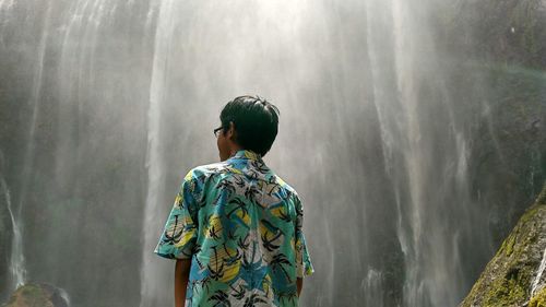 Rear view of man standing against waterfall