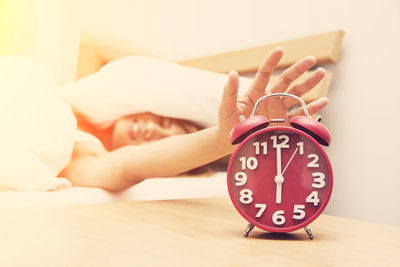 Young woman hand reaching towards alarm clock while sleeping on bed at home