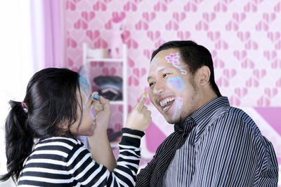 Smiling father and daughter drawing on each other face at home