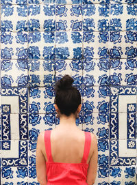 Rear view of woman standing against patterned blue tiled wall