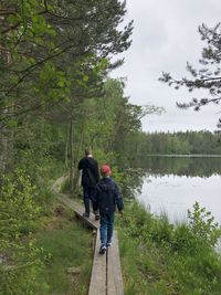 Rear view of boys walking on wooden path by lake