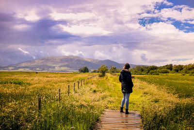 Rear view of girl standing on field against sky