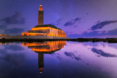 Illuminated building by lake against sky at night