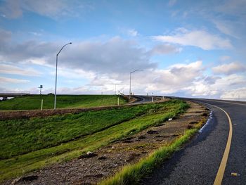 Empty road amidst field against sky