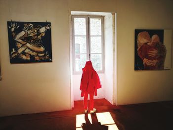 Rear view of woman standing by window at home