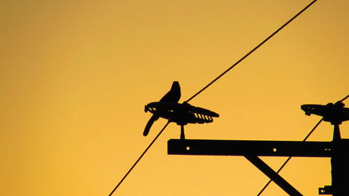 Silhouette bird perching on pole against orange sky