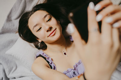 Directly above shot of young woman using smart phone while lying on bed at home
