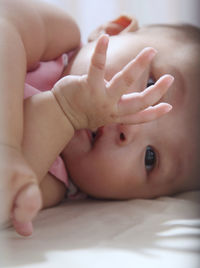 Portrait of cute baby girl with finger in mouth lying on bed