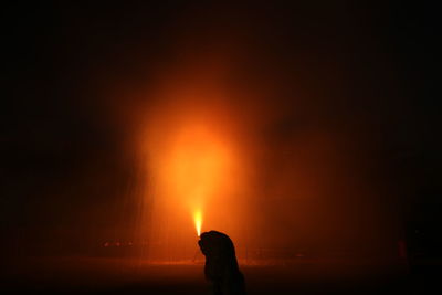 Silhouette people against orange sky at night