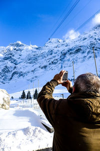 Rear view of man standing on snowcapped mountain against sky