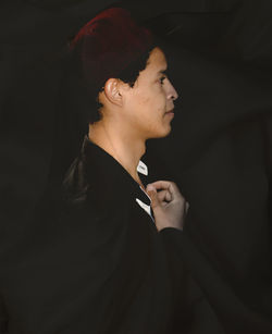 Side view of young man looking away over black background