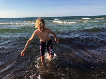 Shirtless boy walking in sea