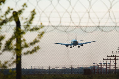 Airplane flying against sky seen through fence