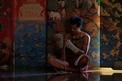 Full length of young man sitting against wall