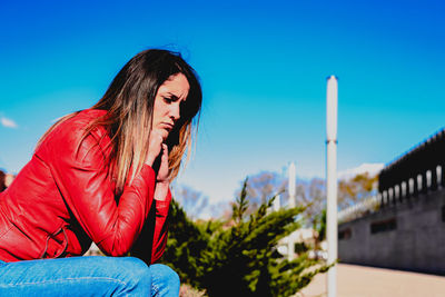 Sad woman sitting against blue sky