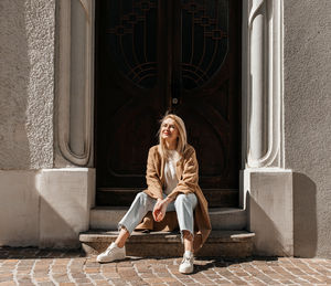 Stylish woman enjoying sunlight while sitting on steps by a vintage door