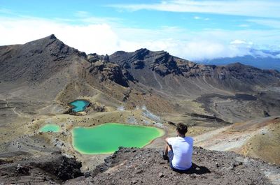 Rear view of man sitting on rock against sky at tongariro national park