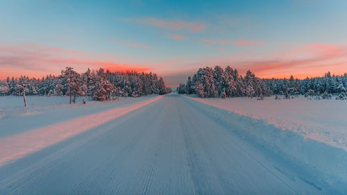 Snow covered road against sky during sunset