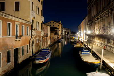 Boats moored in canal amidst buildings in city at night